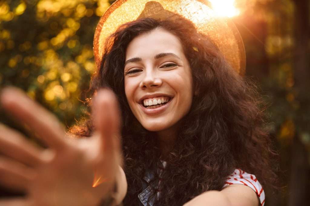 A woman with long curly hair wearing a straw hat and smiling